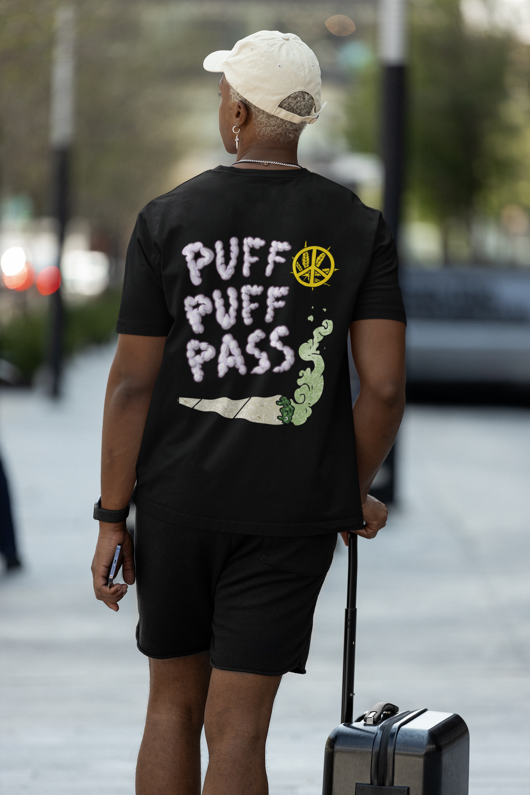 Person wearing a black t-shirt with 'Puff Puff Pass' text and a green snake graphic, walking outdoors.