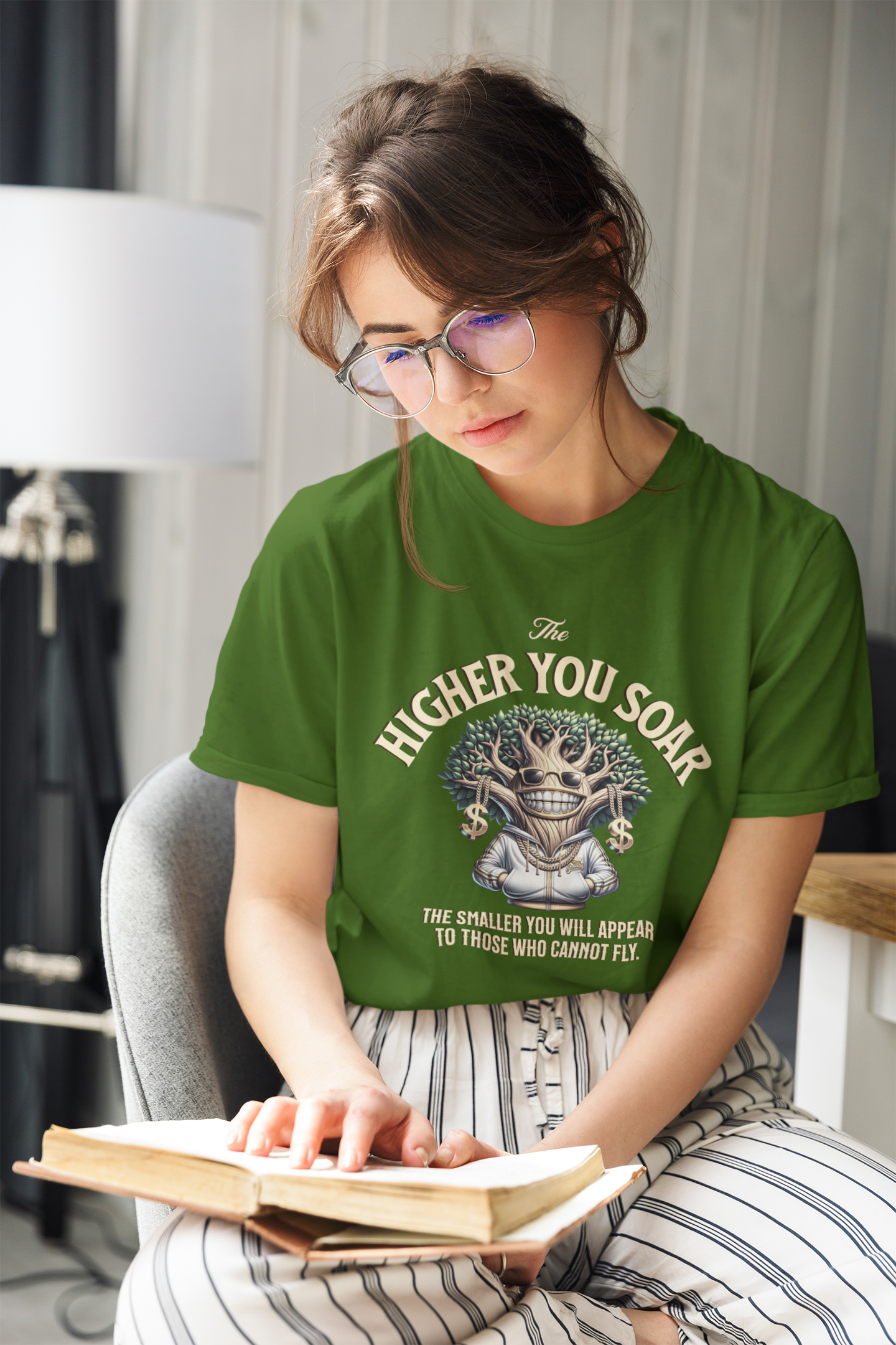 Woman wearing a green t-shirt with a graphic design and text, sitting on a chair reading a book.
