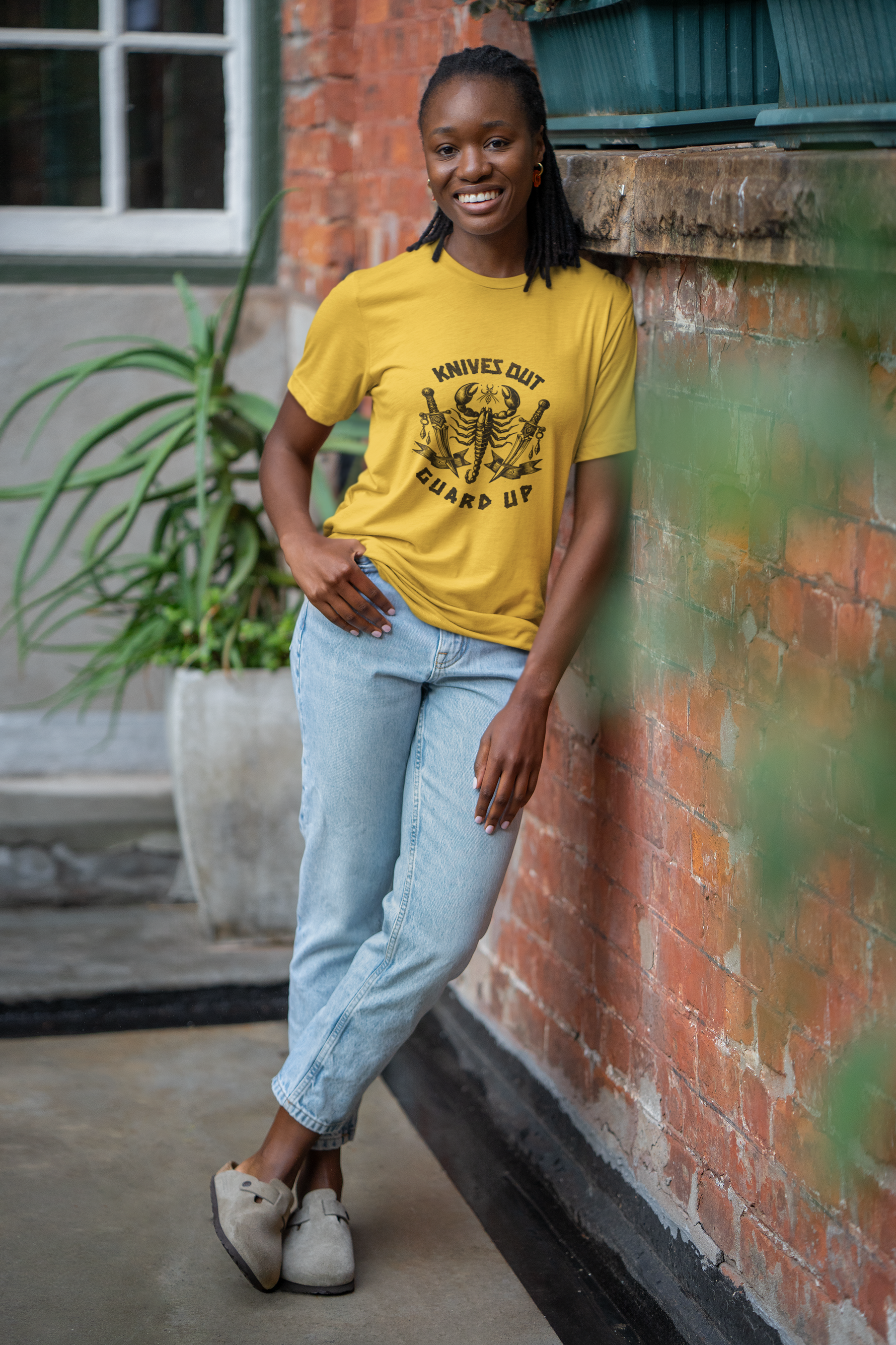 Person wearing a yellow t-shirt with a graphic design, standing against a brick wall.