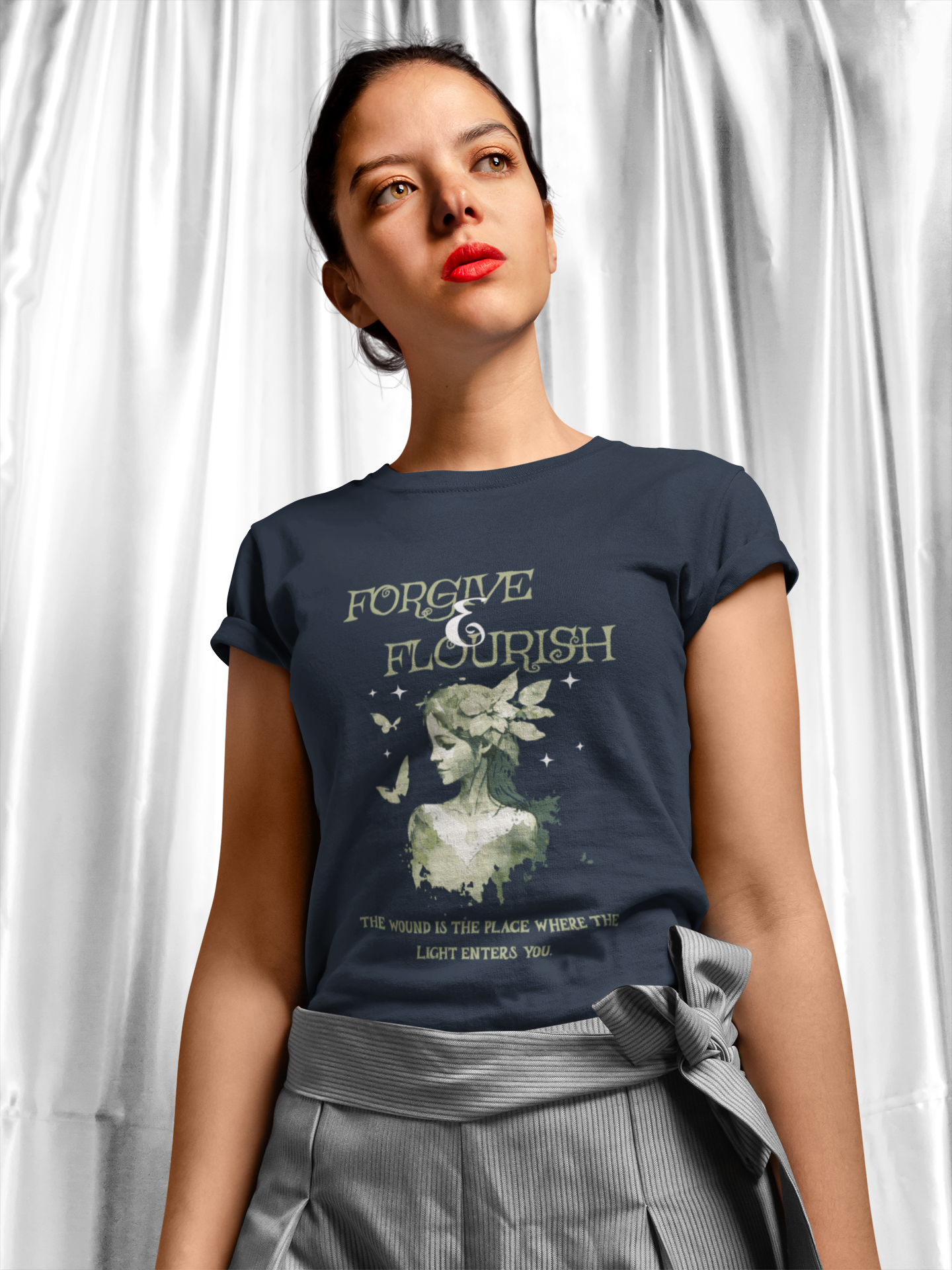 Woman wearing a navy blue t-shirt with a graphic design and text against a white curtain background