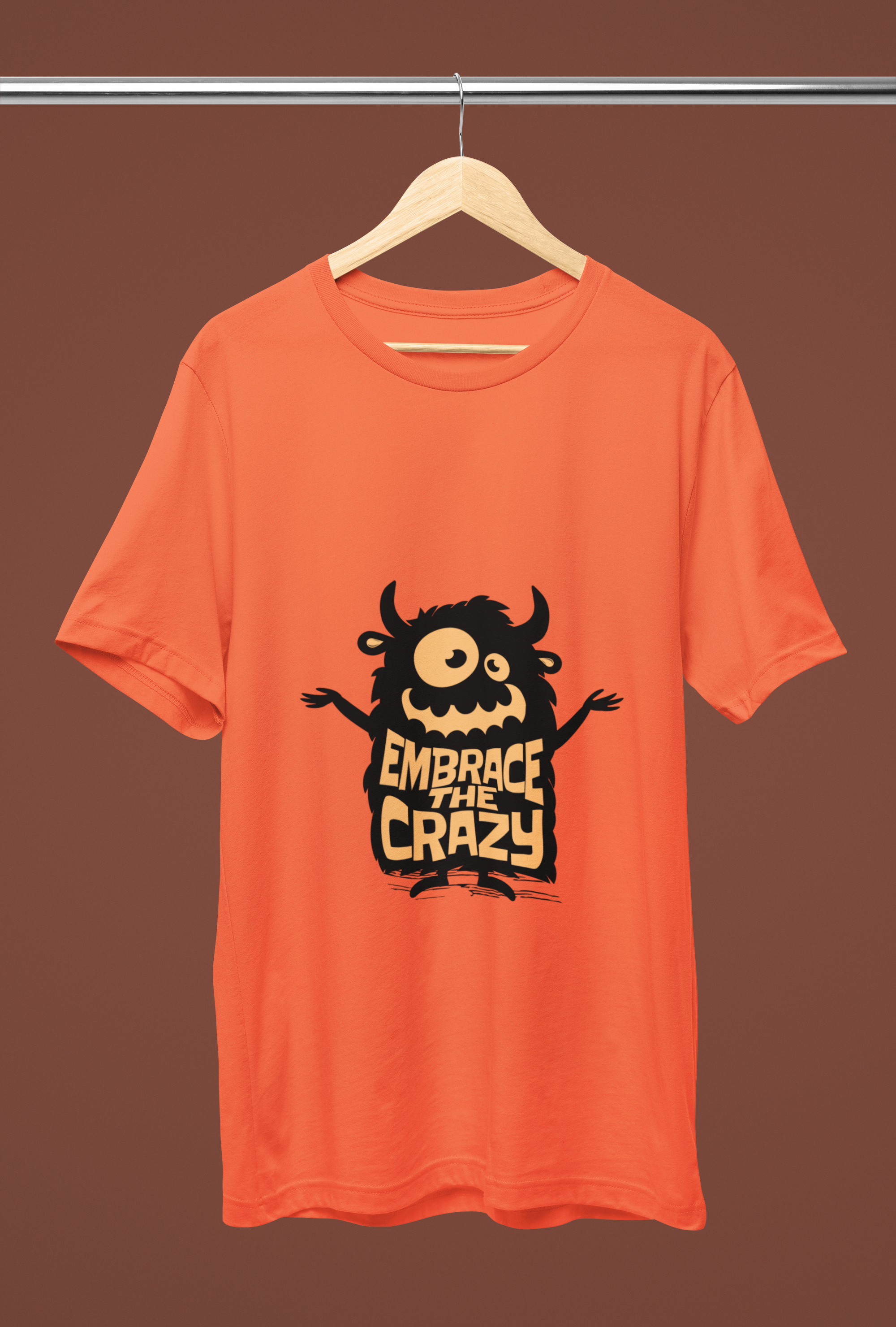 Orange graphic t-shirt with a cute one-eyed monster cartoon and bold text 'Embrace the Crazy' – fun quirky streetwear design.