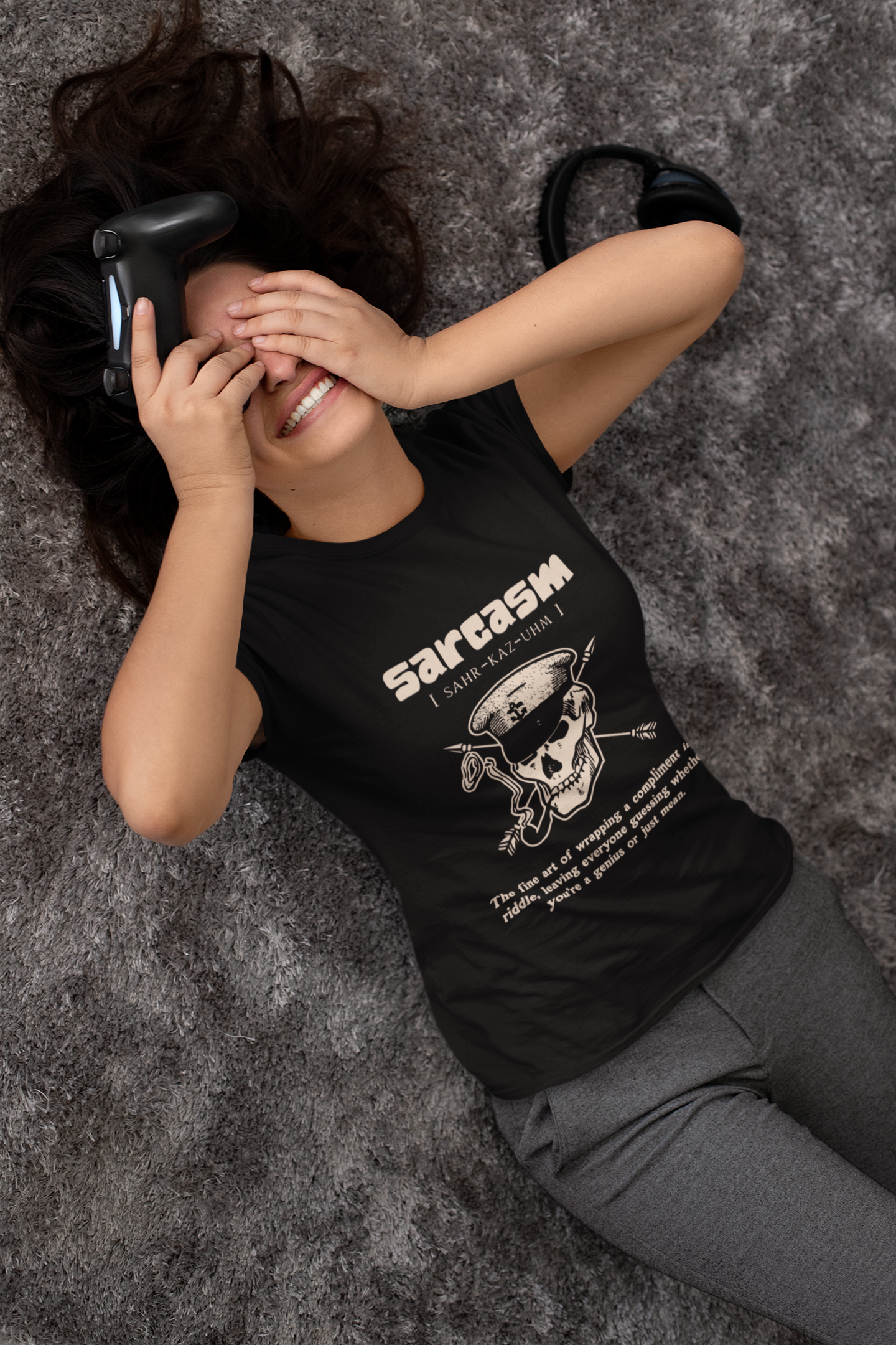 Person wearing a black t-shirt with a graphic design and text, lying on a textured gray surface.