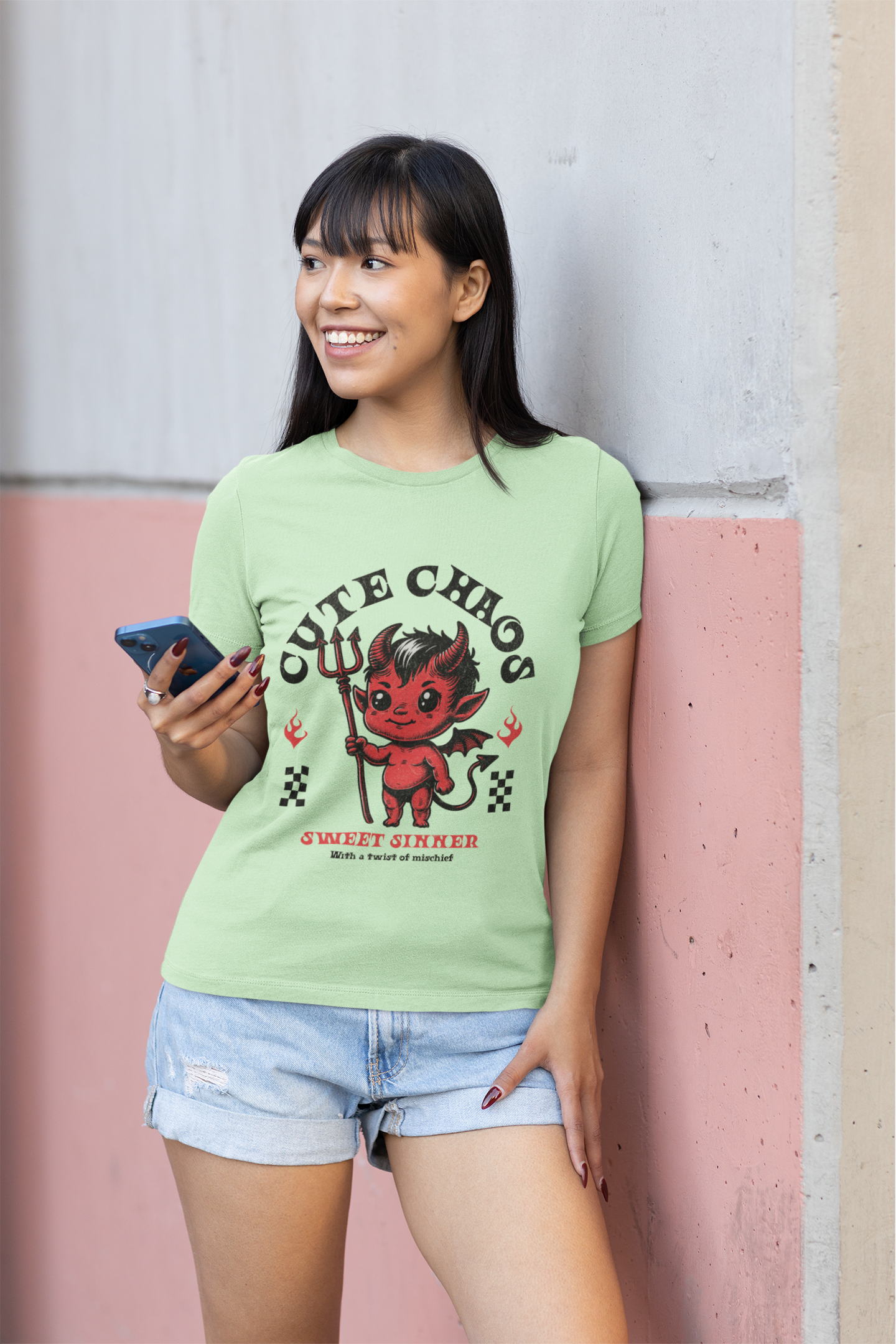 Woman wearing a light green t-shirt with a graphic design, standing against a pink and gray wall.