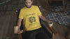 Man wearing a yellow “Wander Often, Wonder Always” Outkast T-shirt while reading and holding coffee, with Instagram call-to-action overlay.
