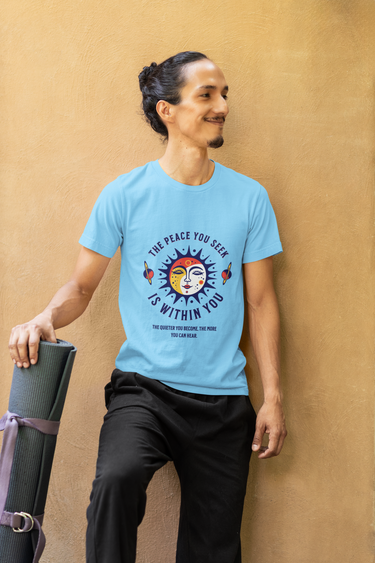 Person wearing a blue t-shirt with a motivational quote, holding a yoga mat against a beige wall.